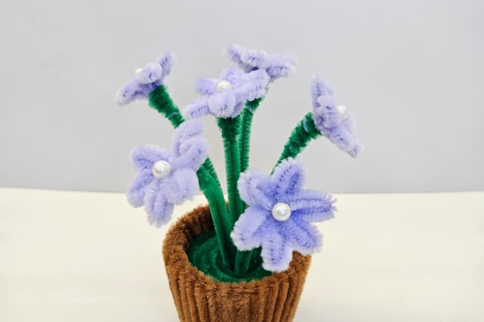 A lavender pipe-cleaner bloom pot with pearl centres, photographed against a pale background